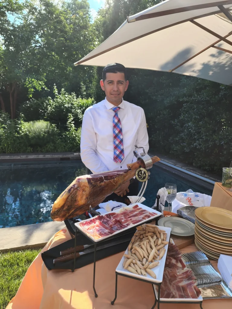 Catering: server beside a jamon iberico cutting station at a poolside catered event