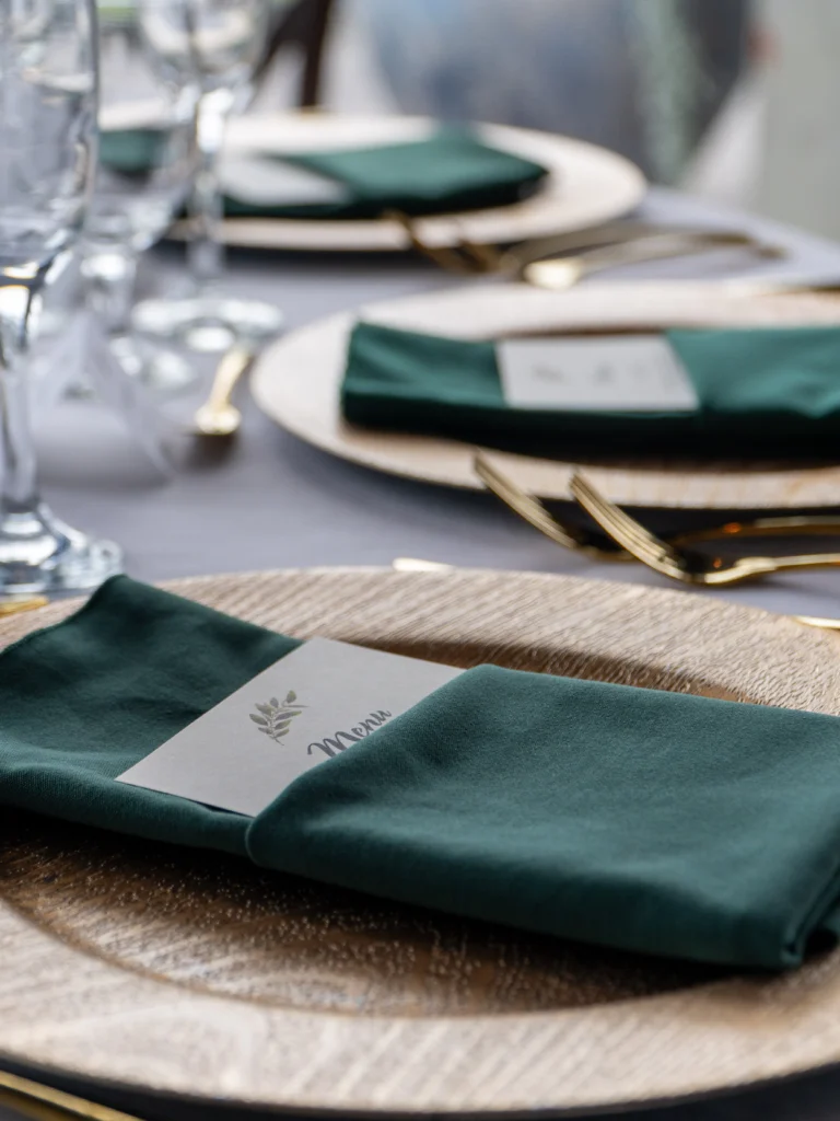 Catering: table setting with green napkins and gold chargers at a wedding