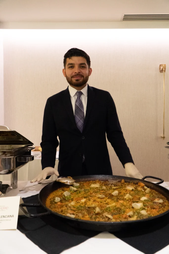 Catering: server standing behind a large pan of paella at a catered event